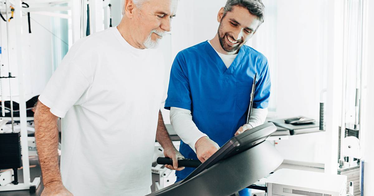 A medical worker and an older man work together as the older man walks steadily on a treadmill while the worker watches.